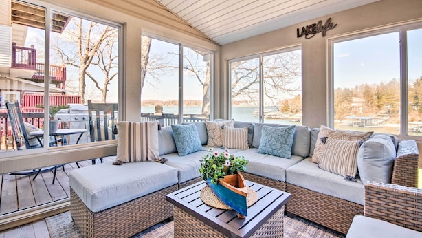 A sunroom with a large window overlooking a lake, a wicker sofa with cushions, and a small table with a plant. - Private Boat Dock: Bright Lake Ozark Home! (Lake Ozark)