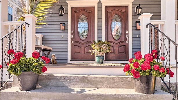 A house with a front porch, two potted plants with red flowers, and a dog sitting on the steps. - New London Hideaway Near Beaches & Local Spots! (New London)