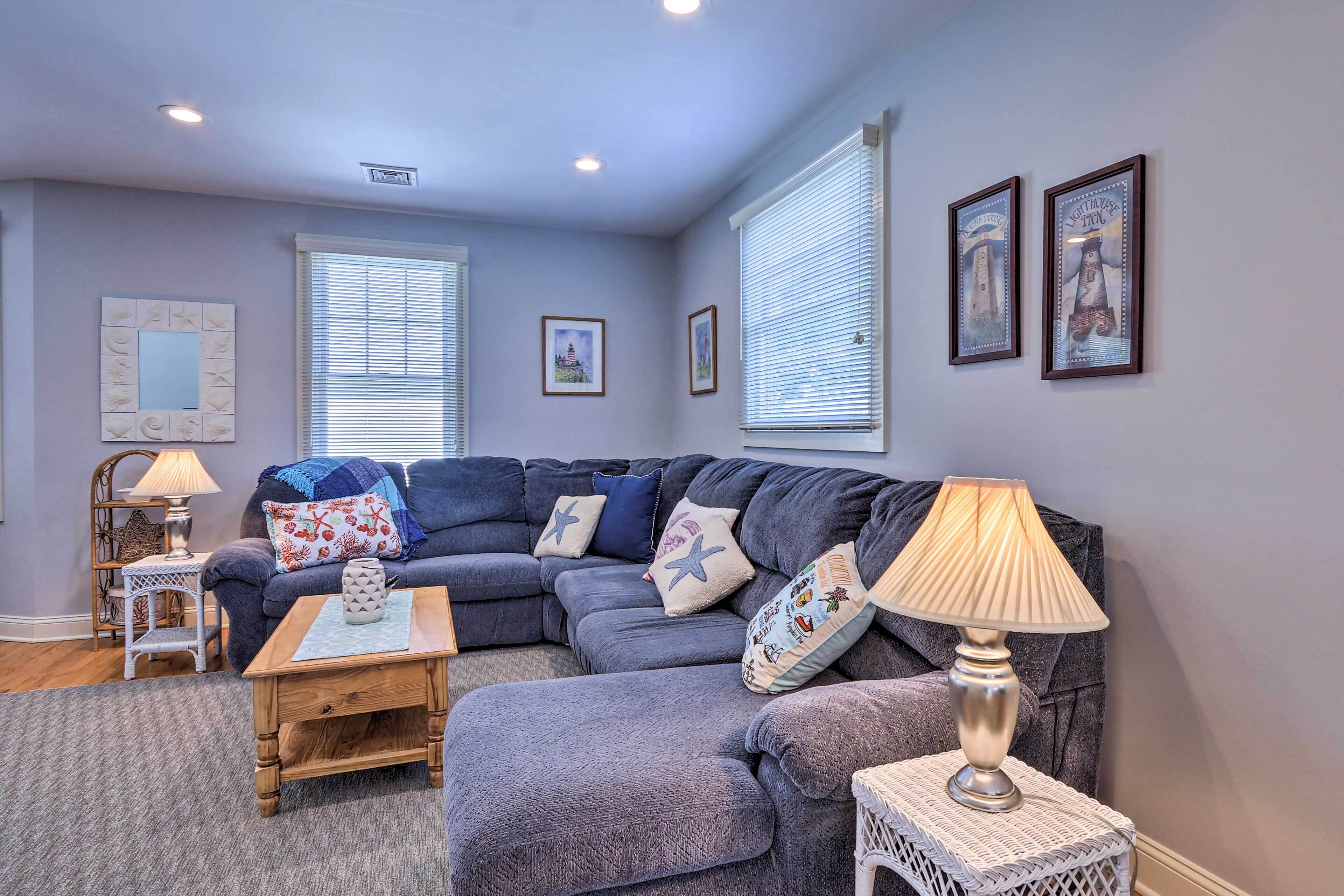A living room with a sectional sofa, a small table, a lamp, and framed pictures on the wall.
