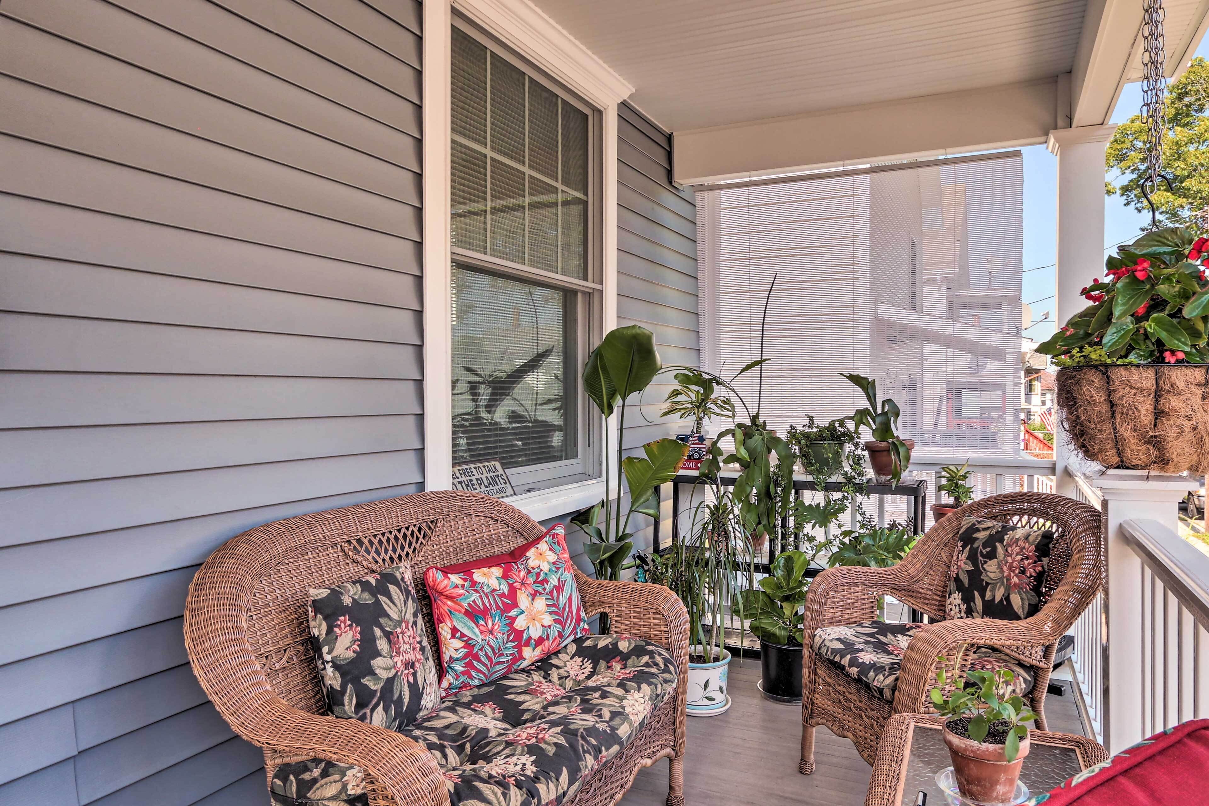 A balcony with wicker furniture, potted plants, and a view of the city.