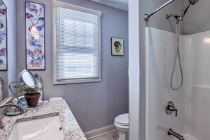A bathroom with a sink, toilet, and shower. There is a window with blinds, a potted plant, and a framed picture on the wall. - New London Hideaway Near Beaches & Local Spots! (New London)