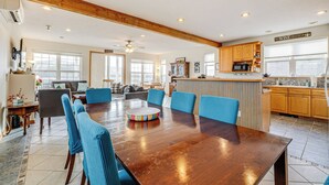Un comedor amplio con una mesa de madera y sillas azules, una cocina con armarios de madera y un ventilador de techo.