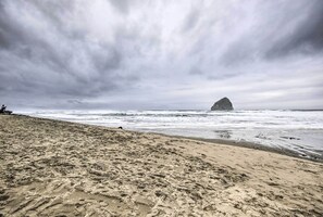 A beach with footprints leading to the water, a large rock formation in the distance, and a cloudy sky.