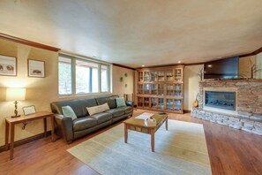 A living room with a leather sofa, wooden coffee table, stone fireplace, and a bookcase. - Homey Mtn View Escape: 11 Mi to Garden of the Gods (Cascade)