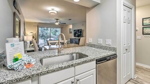 A modern kitchen with granite countertops, a built-in dishwasher, and a dining area with a ceiling fan. - Renovated Gem w/ Pool Access: 1/4 Mi to Beach (Santa Rosa Beach)