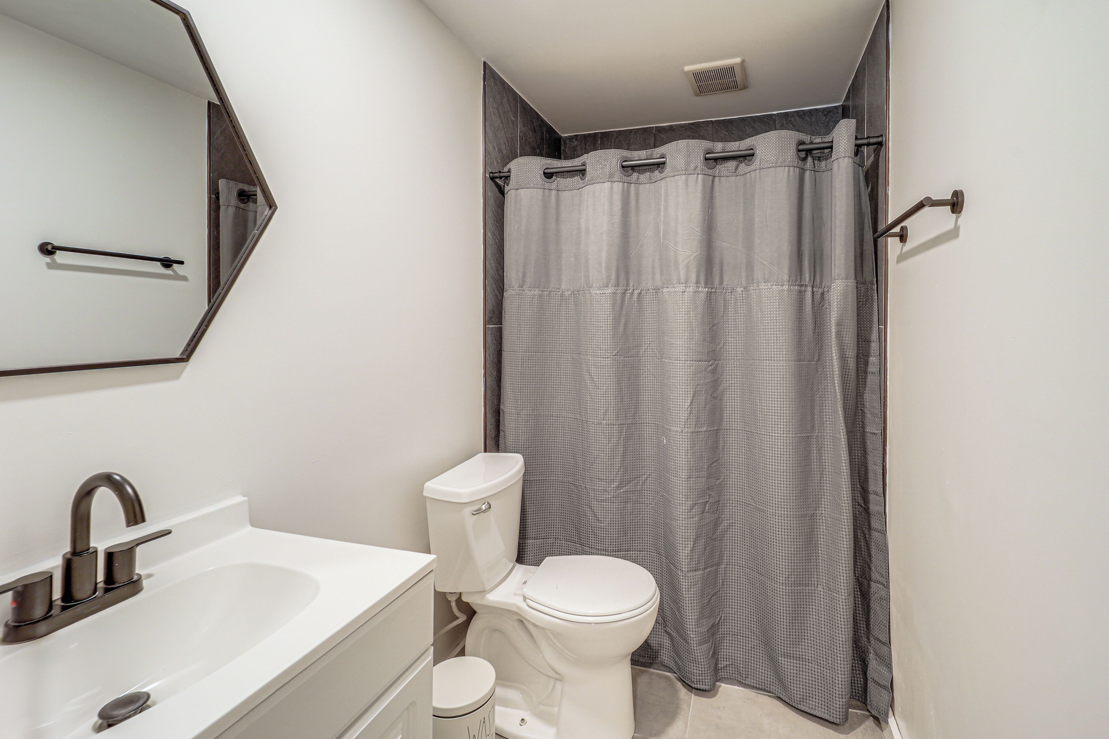 Une salle de bain avec un lavabo blanc, des toilettes, un miroir et un rideau de douche.