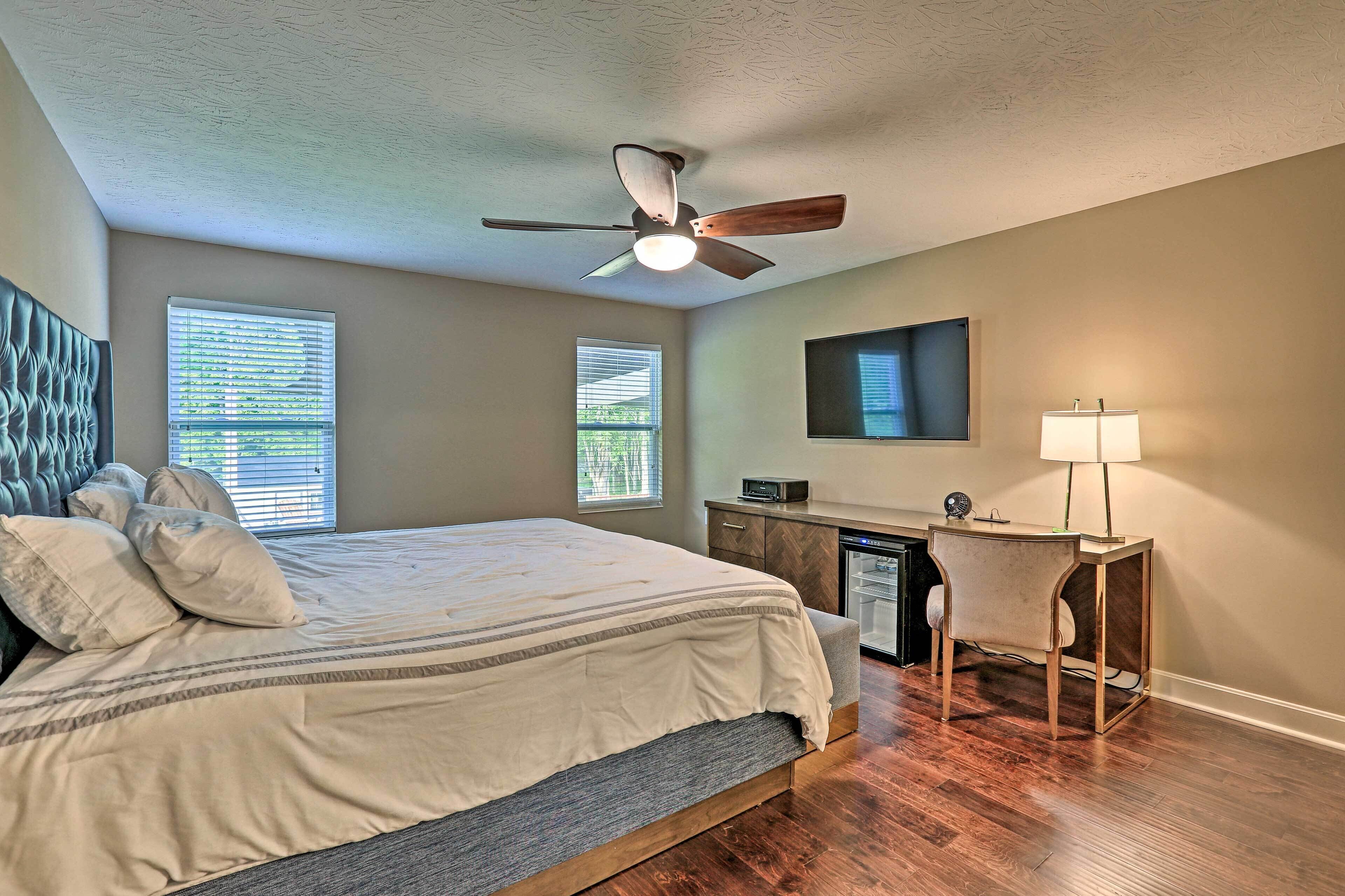 A bedroom with a bed, a desk, a chair, a ceiling fan, and two windows.