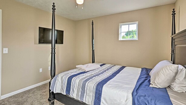A bedroom with a four-poster bed, a ceiling fan, a television mounted on the wall, and a window providing natural light. - Spacious Family Home w/ Fire Pits, Large Yard (Goshen)