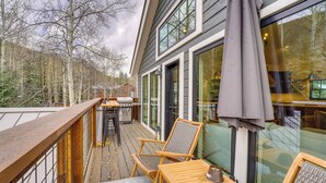 Eine Holzterrasse mit Sitzgelegenheiten im Freien, einem Grill und Blick auf Bäume.