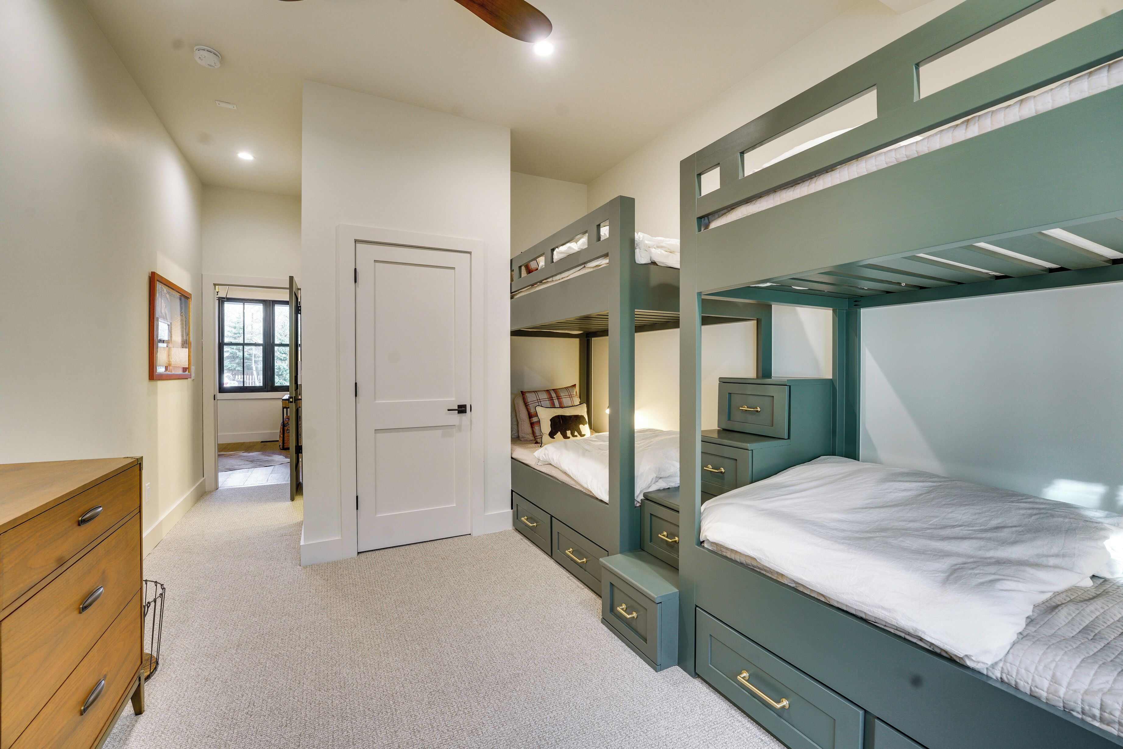 Une chambre avec des lits superposés, une commode et une porte donnant sur une autre pièce.