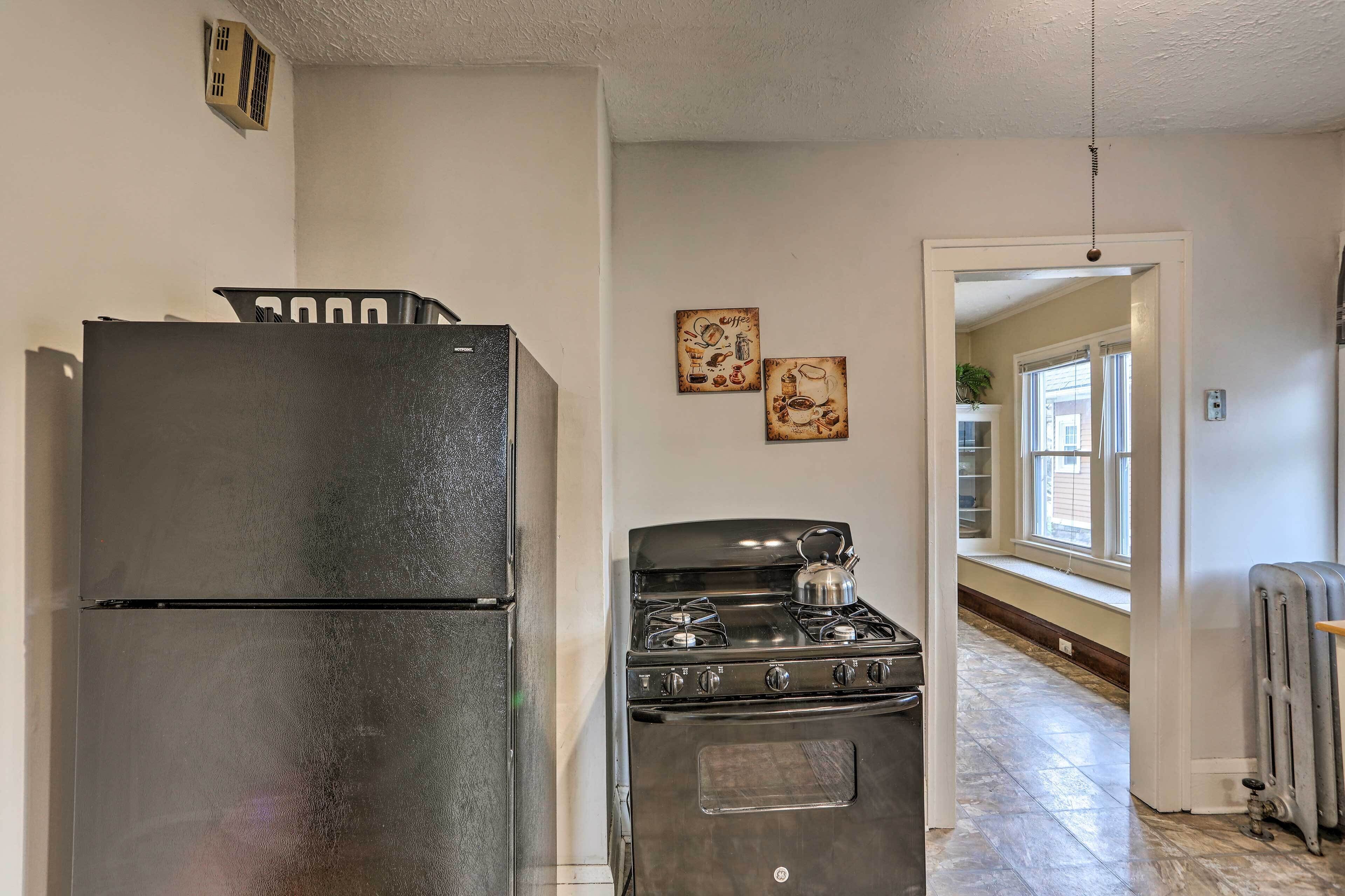 A kitchen with a refrigerator, stove, and oven. There are two wall decorations and a radiator on the floor.