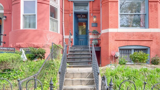 Un bâtiment en briques rouges, avec une porte bleue et un escalier menant à l’entrée.