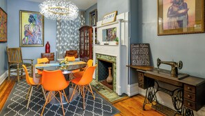 Un espace repas avec une table ronde, des chaises orange, un lustre et une cheminée.
