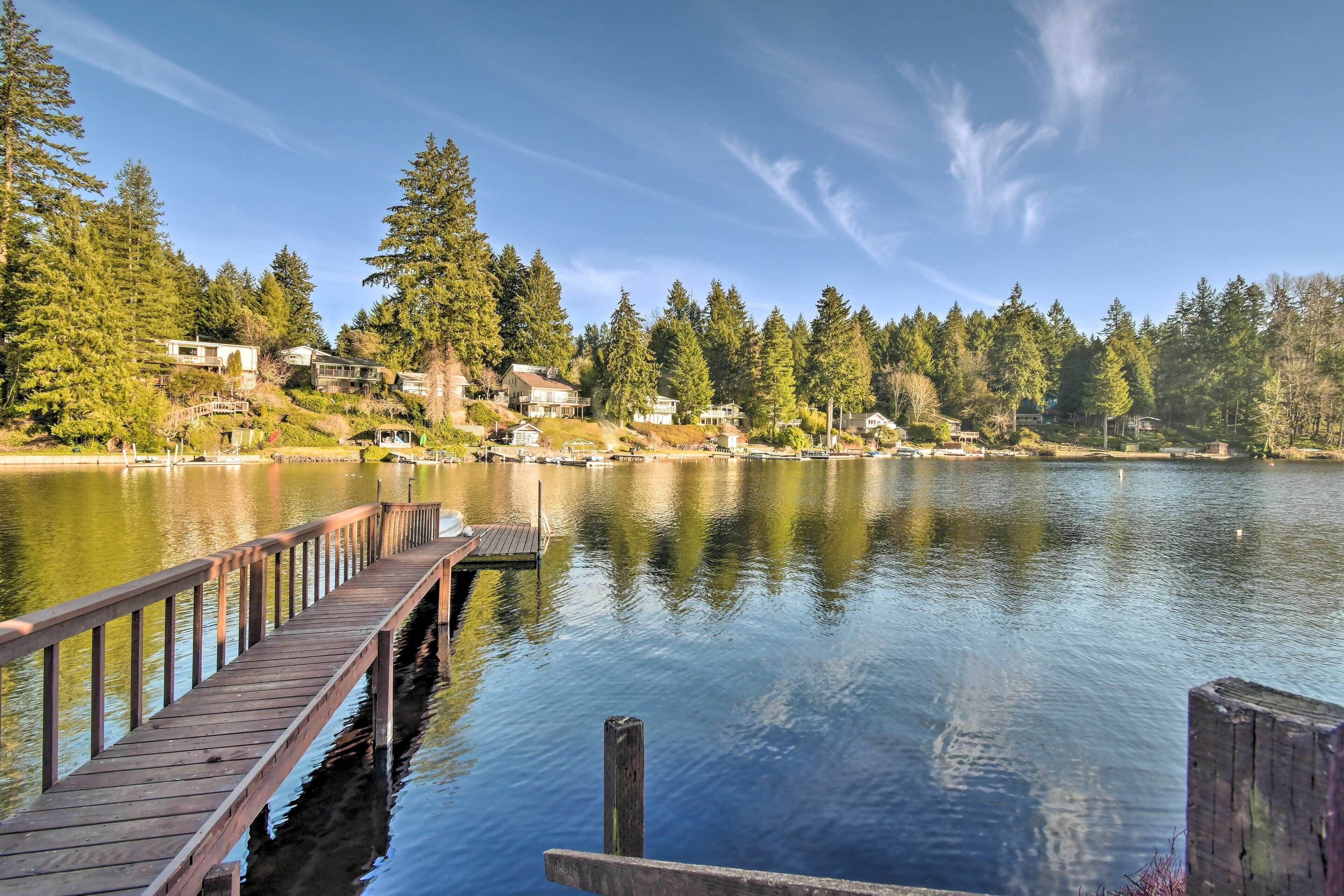 A wooden pier extending into calm water, surrounded by dense forest and houses.