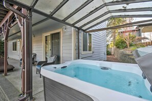 Een overdekt buitengebied met een jacuzzi, tuinmeubilair en een huis op de achtergrond.