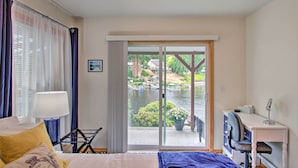 Une chambre d’hôtel avec un lit, un bureau et une chaise, une lampe, et une vue sur un lac où l’on peut voir des bateaux.