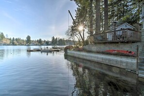 Een pand aan het water met een steiger, een huis met terras, en een bebost gebied.