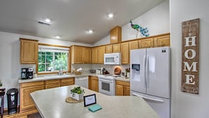 Une cuisine moderne avec des meubles en bois, un réfrigérateur blanc, un four à micro-ondes et un grand îlot central doté d’une tablette et d’une plante.