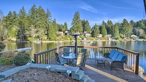 Une terrasse en bois, agréée de mobilier d’extérieur, qui offre une vue sur un lac, avec des maisons en arrière-plan.