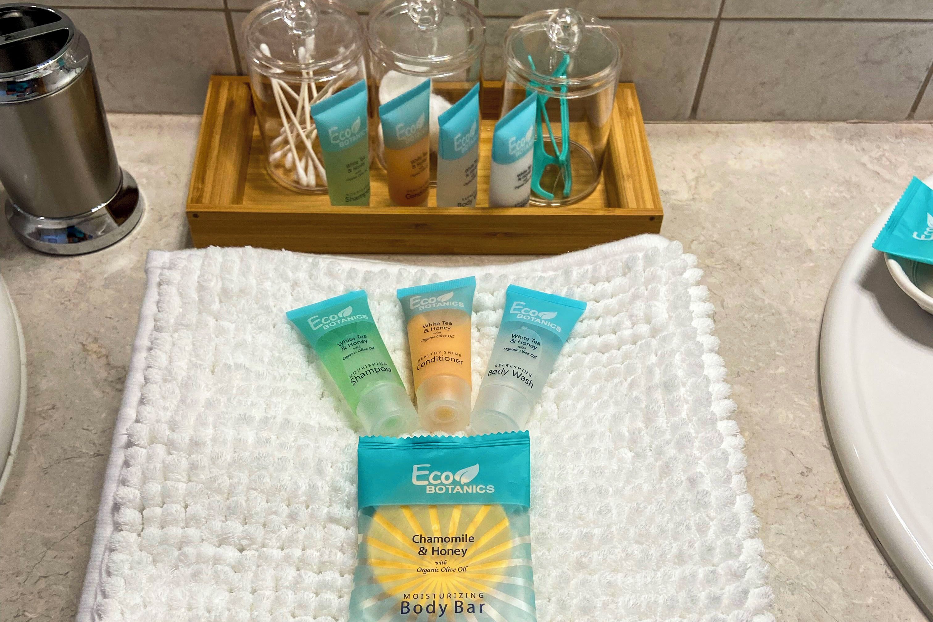 A bathroom with a white towel, a tray of toiletries, and a bottle of body bar.