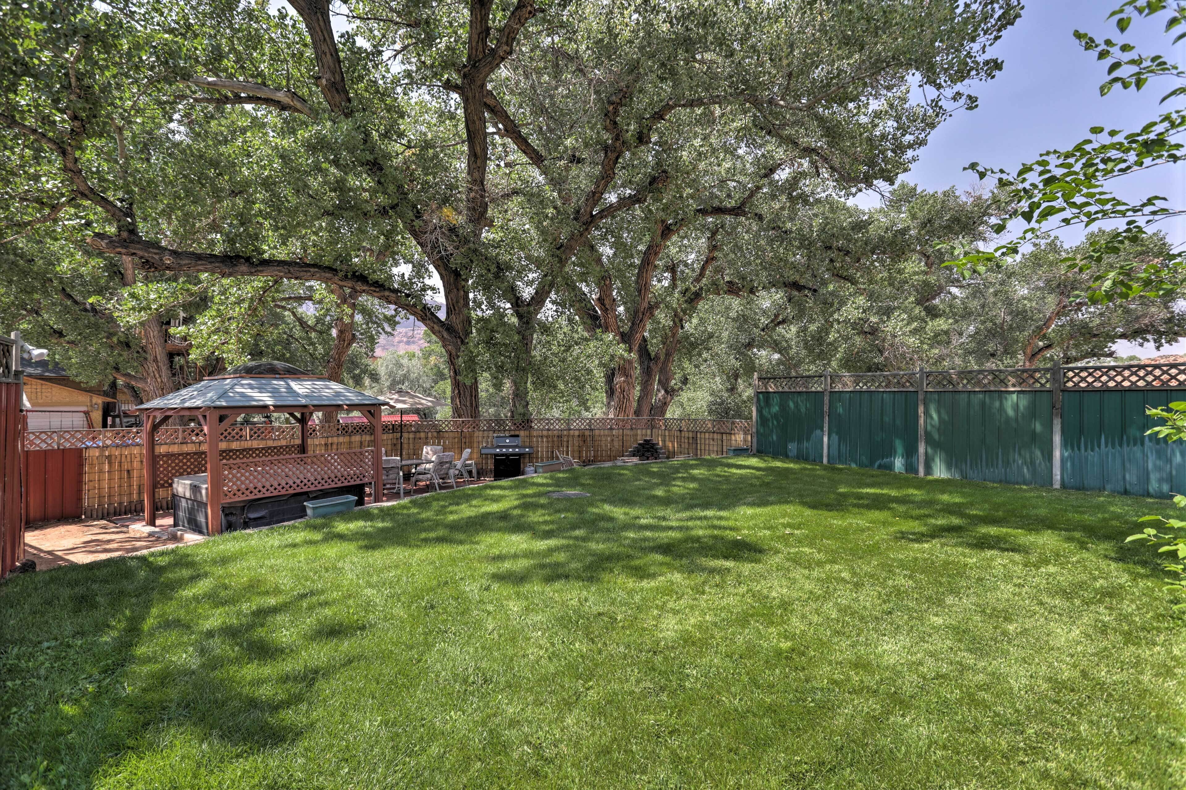 A backyard with a wooden pergola, a barbecue grill, and a fenced area with trees.