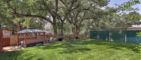 A backyard with a wooden pergola, a barbecue grill, and a fenced area with trees.