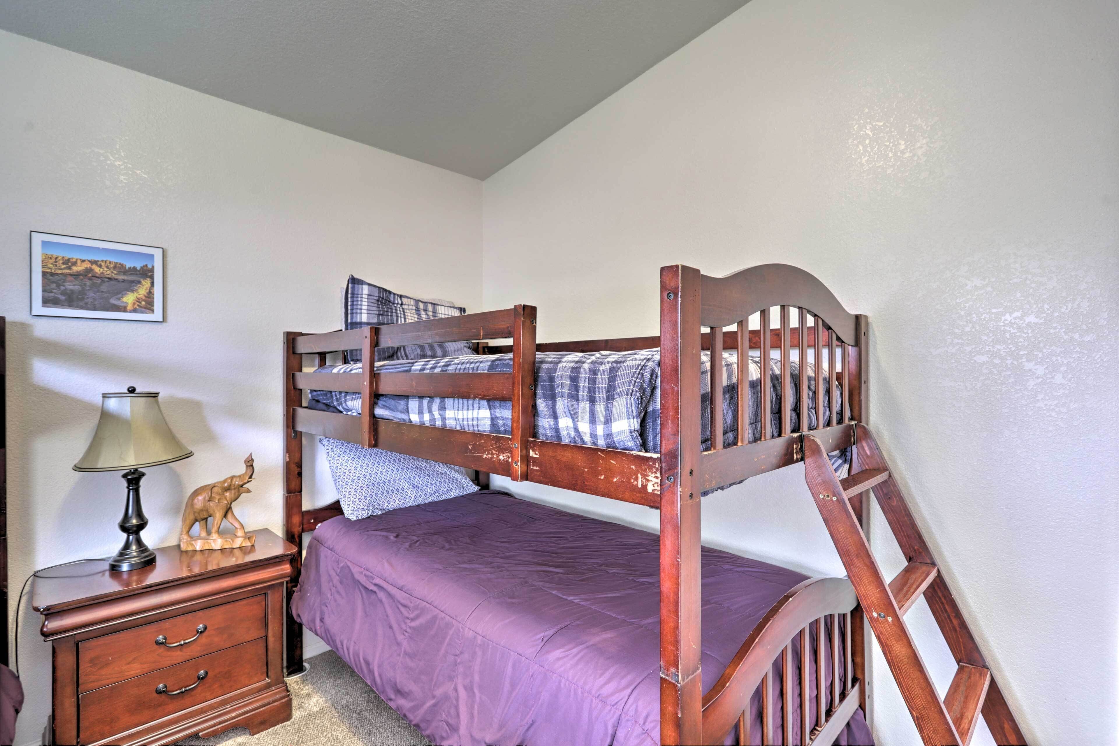 A bunk bed with a wooden frame, a purple mattress, and a nightstand with drawers and a lamp.