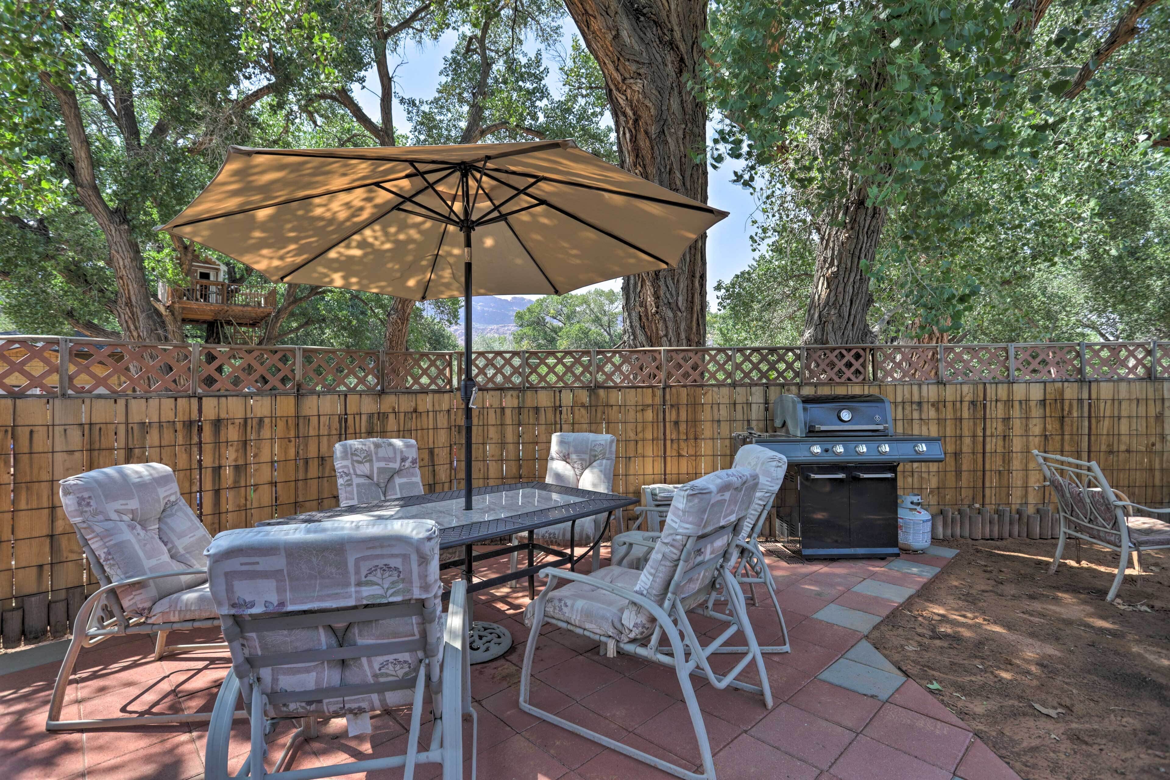 An outdoor patio with a table, chairs, and a grill.