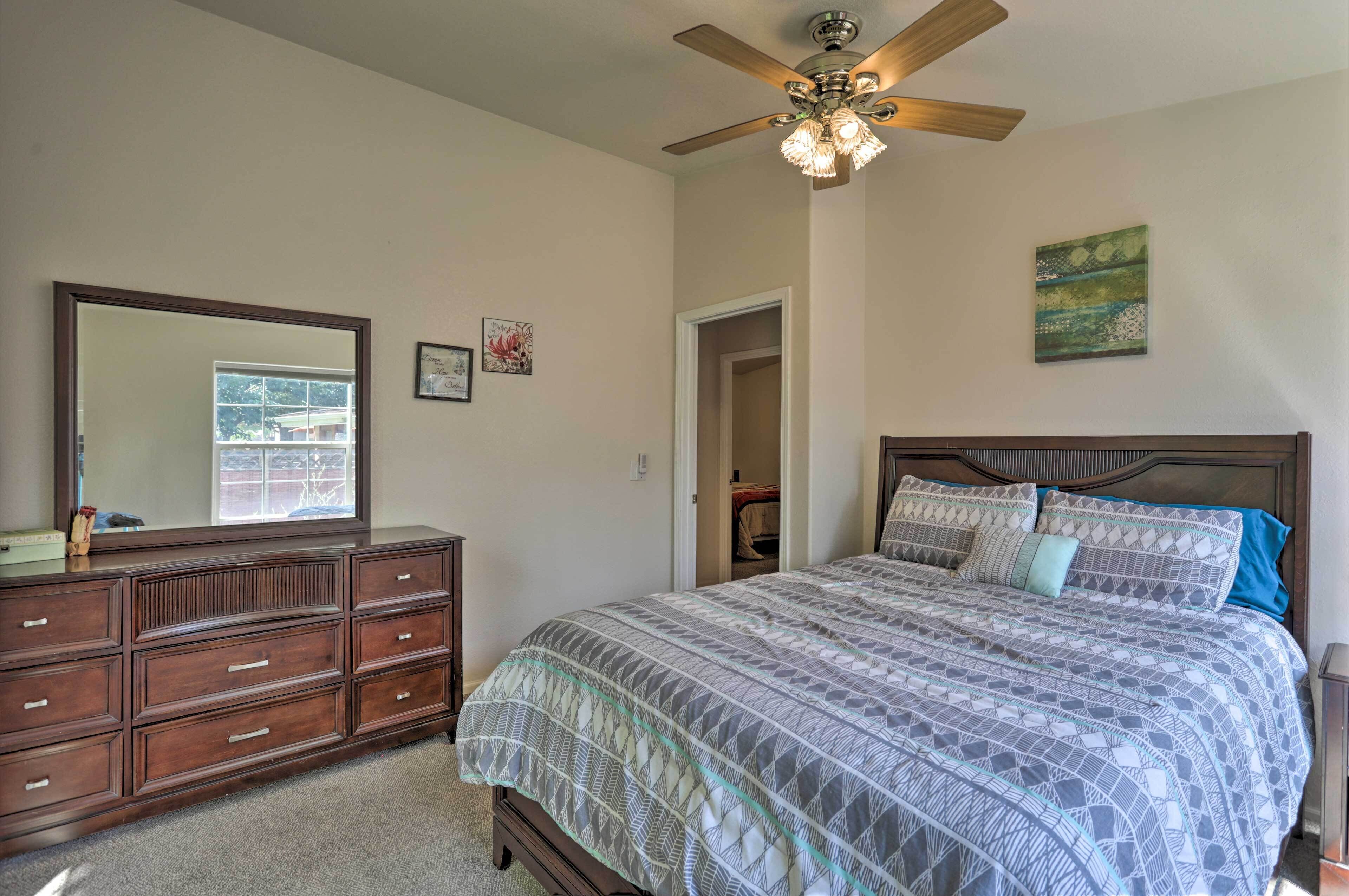 A bedroom with a bed, dresser, ceiling fan, and artwork on the walls.