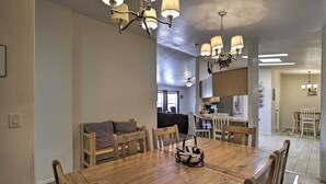 A dining area with a wooden table, chairs, and a chandelier. There is a kitchen in the background with cabinets and a countertop. - 'rustic Retreat' Moab Townhome w/ Grill & Fire Pit (Moab)