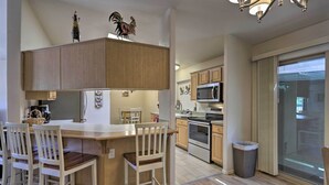 A kitchen with wooden cabinets, a microwave, an oven, and a dining area with chairs. - 'rustic Retreat' Moab Townhome w/ Grill & Fire Pit (Moab)