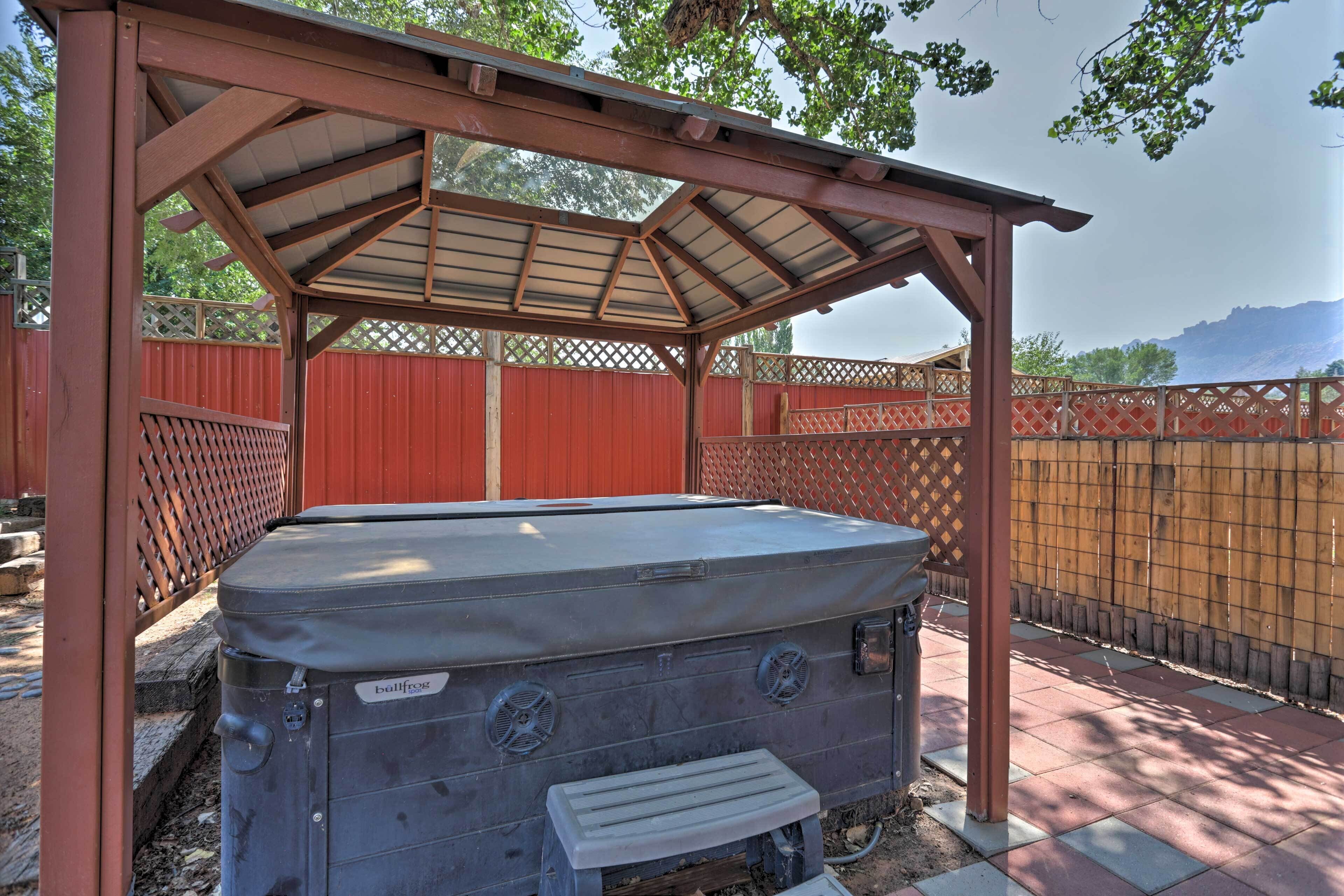 A hot tub under a wooden pergola in a fenced backyard.