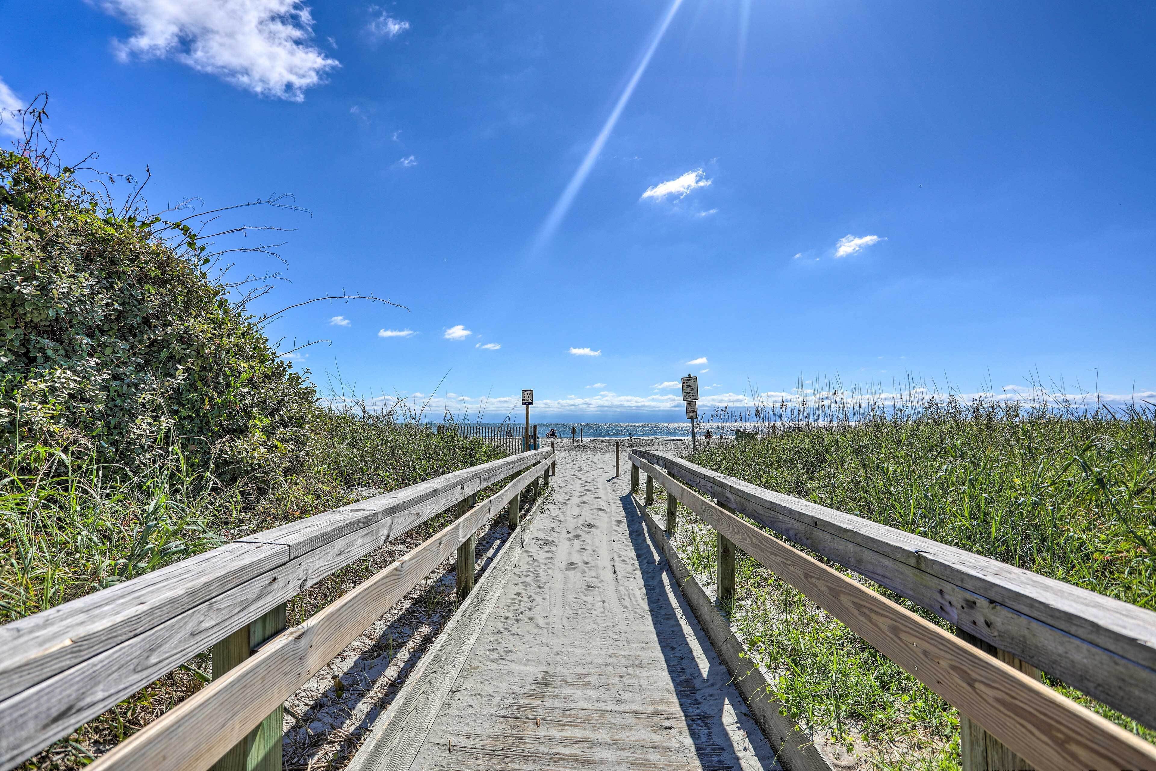 A wooden boardwalk leading to a beach with a clear sky and distant mountains.