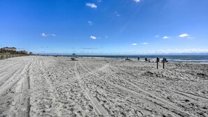 Ampia spiaggia sabbiosa con impronte che si inoltrano verso l'oceano, alcune persone e un edificio sullo sfondo.