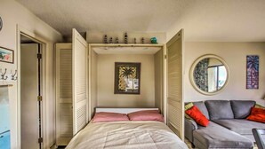 Una camera da letto con un letto, un divano grigio, uno specchio rotondo e un quadro appeso al muro.