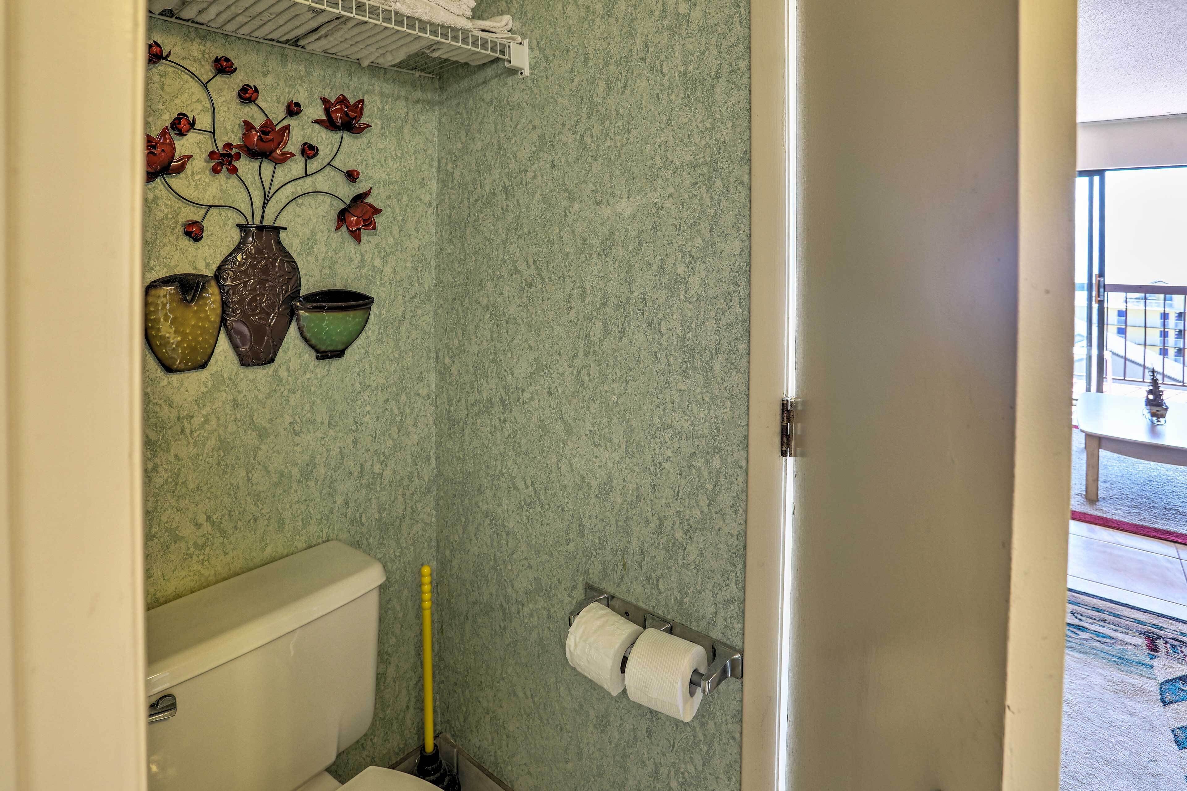 A bathroom with a toilet, a toilet paper holder, and decorative vases on the wall.