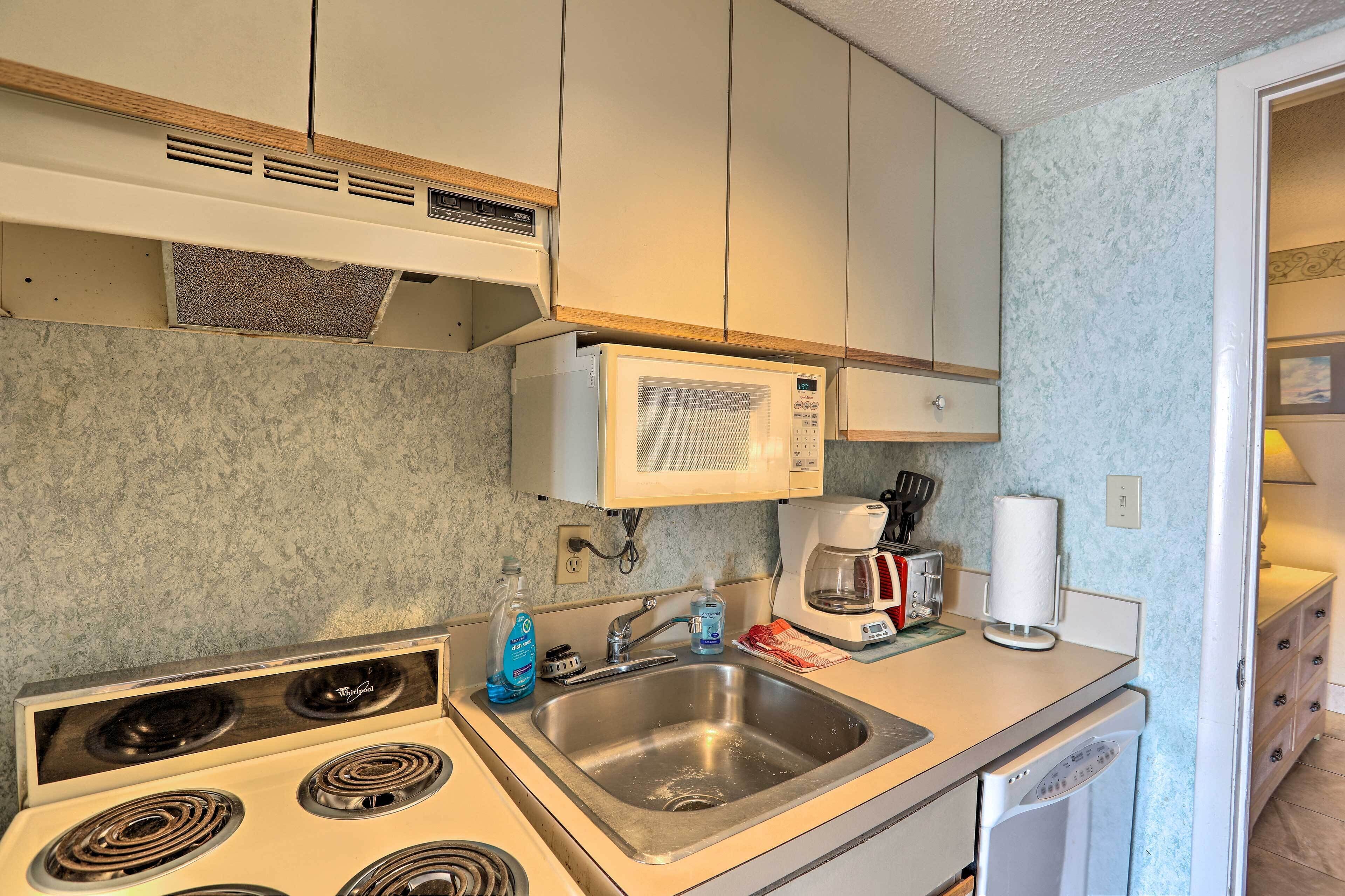 A compact kitchen with a microwave, stove, sink, and a coffee maker.