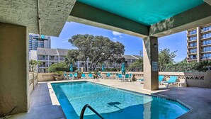 Una piscina con lettini e una zona coperta, circondata da edifici e alberi.