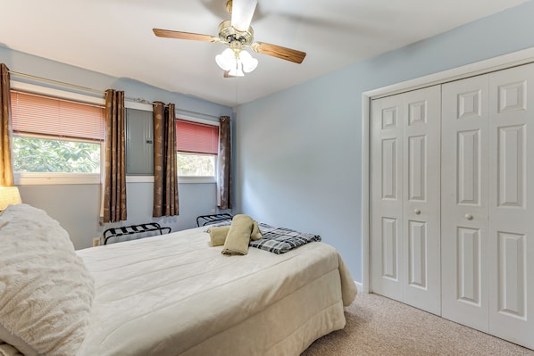 A bedroom with a bed, a ceiling fan, a window with curtains, and a wardrobe.