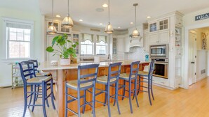 A kitchen with white cabinets, a central island with bar stools, pendant lighting, and a potted plant. - Spacious Avalon Beach House - 2 Blocks to Water! (Avalon)