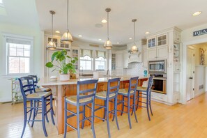 A kitchen with white cabinets, a central island with bar stools, pendant lighting, and a potted plant. - Spacious Avalon Beach House - 2 Blocks to Water! (Avalon)