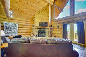 A log cabin interior with a stone fireplace, leather sofa, and wooden walls. - Gatlinburg Cabin w/ Mtn-view Deck ~ 11 Mi to Dtwn (Gatlinburg)
