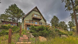 A two-story house with a balcony, surrounded by trees and a grassy area. - Stunning Evergreen Chalet w/ Private Hot Tub! (Evergreen)