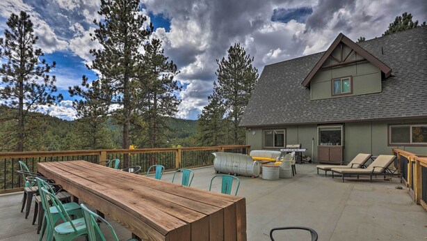 A wooden deck with a long table and chairs, a barbecue grill, and lounge chairs. - Stunning Evergreen Chalet w/ Private Hot Tub! (Evergreen)