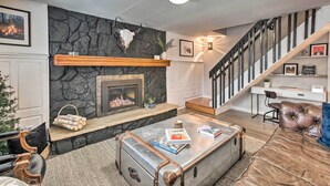 A living room with a fireplace, a staircase, and a desk with a computer. - Stunning Evergreen Chalet w/ Private Hot Tub! (Evergreen)