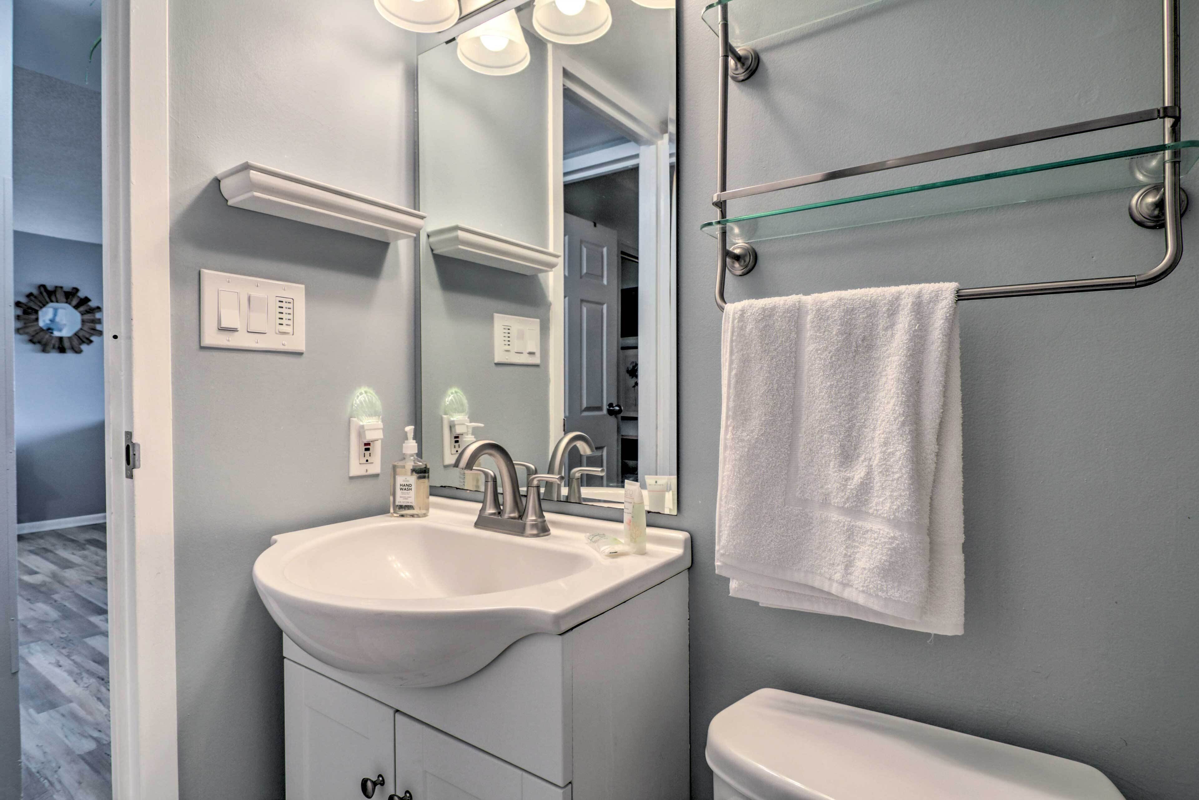 A bathroom with a white sink, a mirror, a towel rack, and a glass shelf.