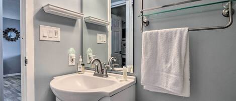 A bathroom with a white sink, a mirror, a towel rack, and a glass shelf.