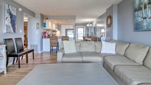 Ein geräumiges Wohnzimmer mit einer großen beigefarbenen Couch, einem Essbereich mit Korbstühlen und einer Küche im Hintergrund.