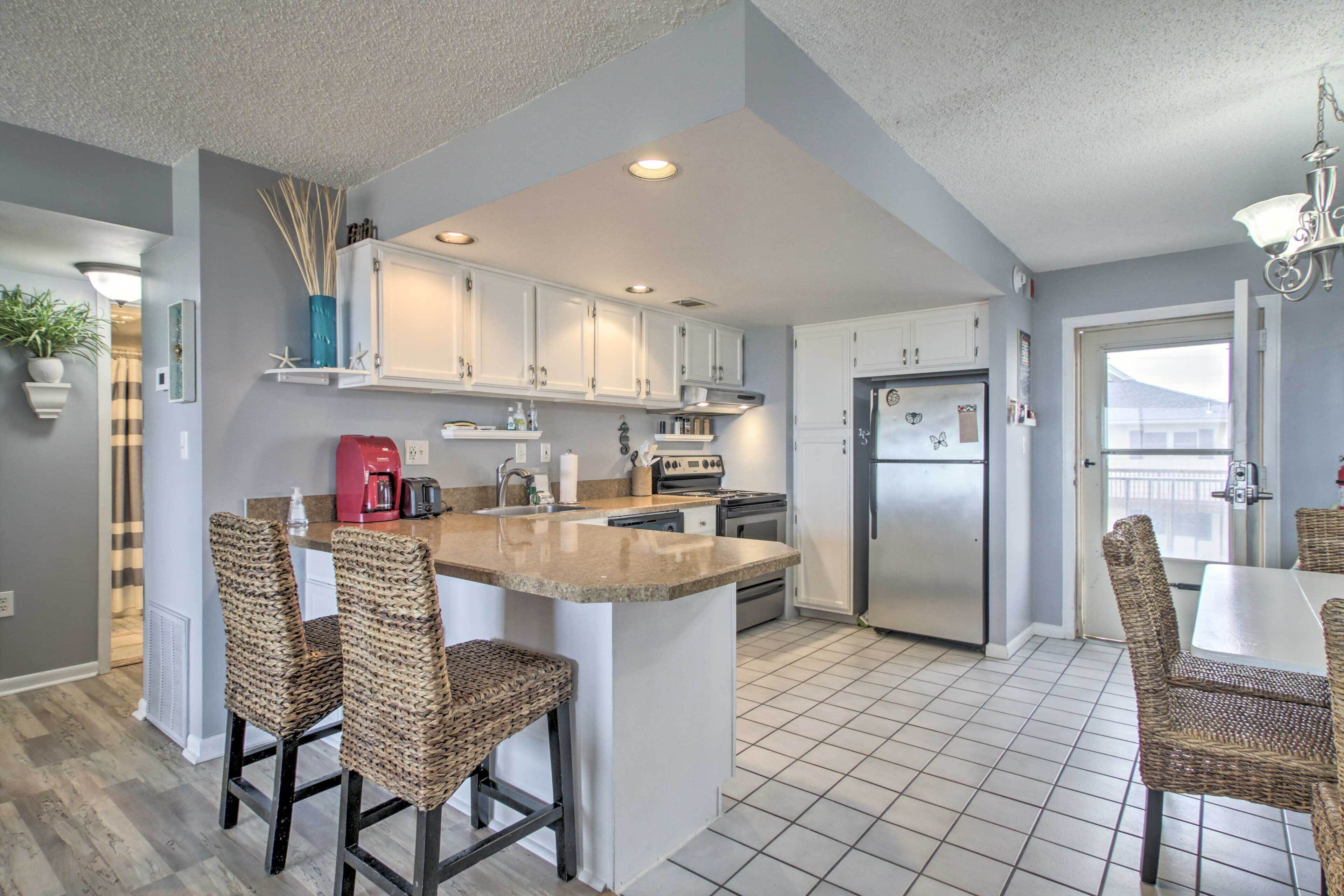 A modern kitchen with white cabinets, a central island, and wicker chairs.