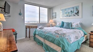 Ein Schlafzimmer mit einem großen Bett, einem Schreibtisch, einem Stuhl, einem Fenster mit Blick und einem Bild an der Wand.